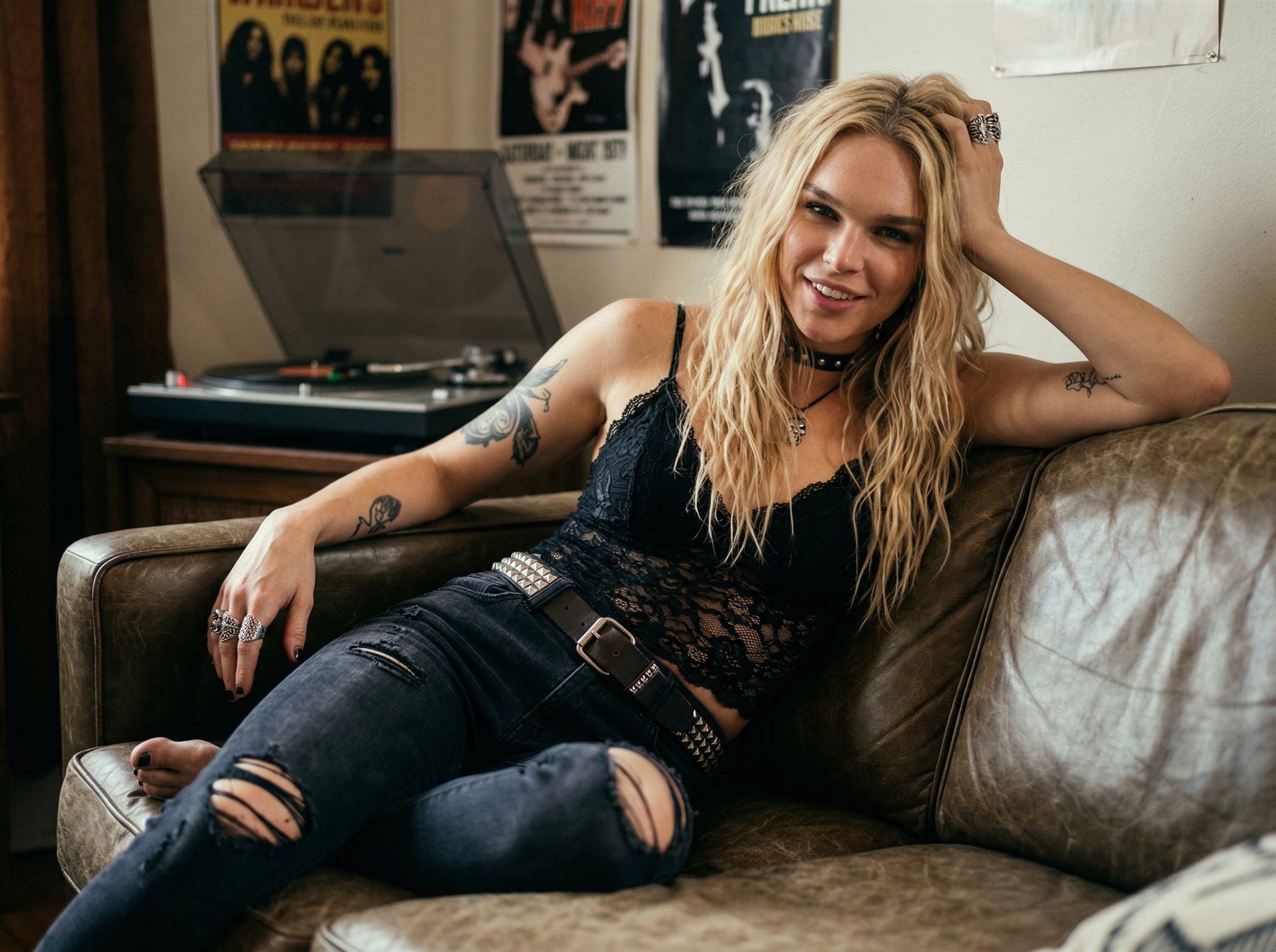 Elin Skär smiling on a leather couch in front of a record player and band posters